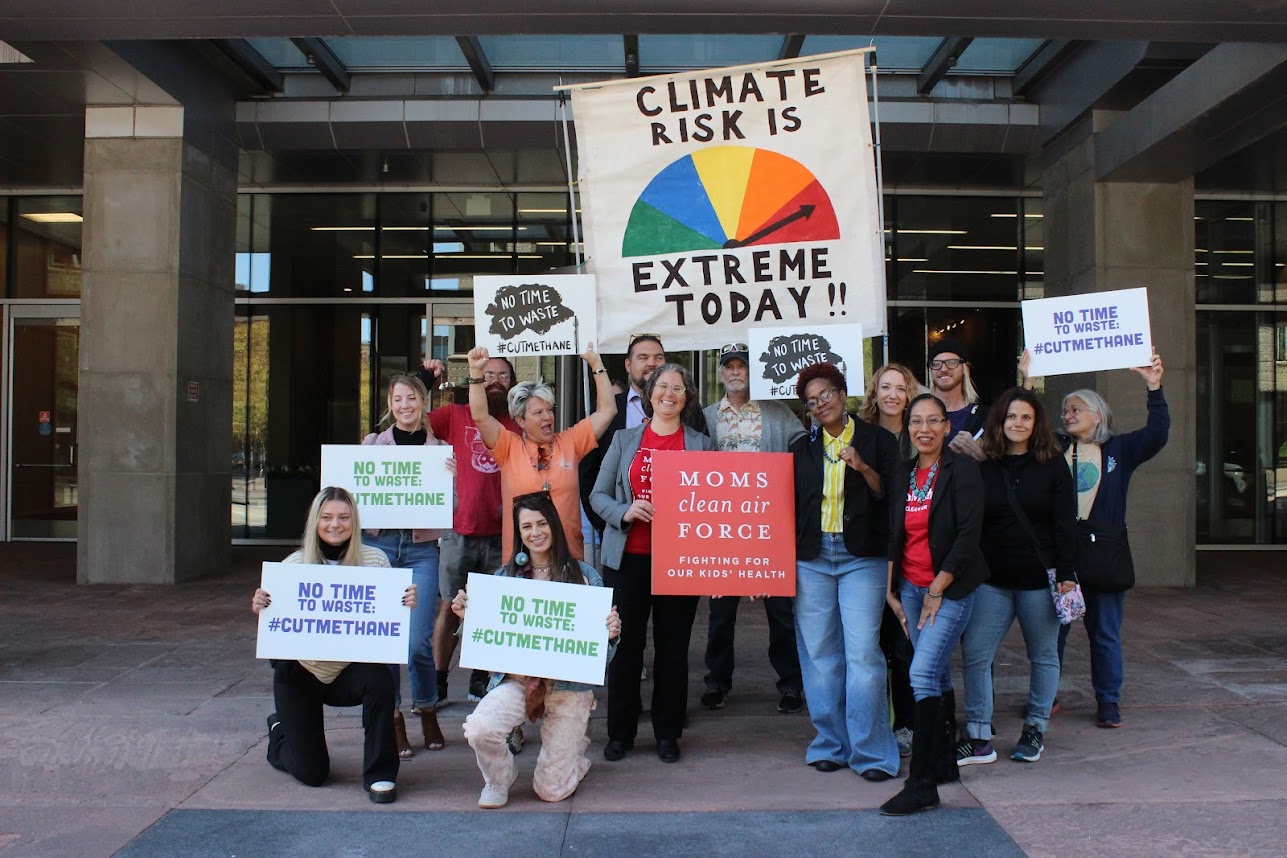 Much Ado About Methane Group Photo, fourteen people holding signs that say things like 'climate risk is extreme today' that resembles a fire danger arrow and scale.